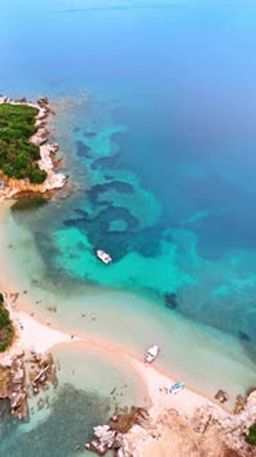 Descending above the sandy beach surrounded by mountains. Very few people walk by the shore.