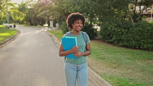 Young afro-american student joyfully walking in slow motion along a campus path