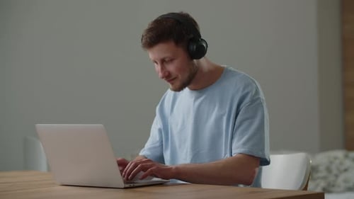 Young Man Works on Laptop with Headphones
