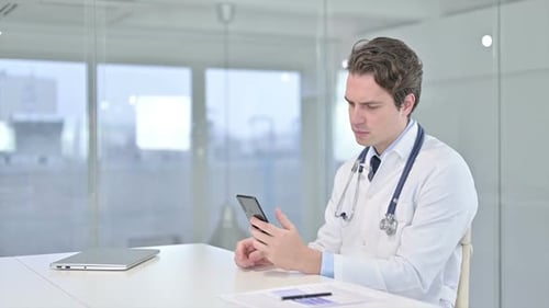 Attractive Young Male Doctor Using Smartphone in Office