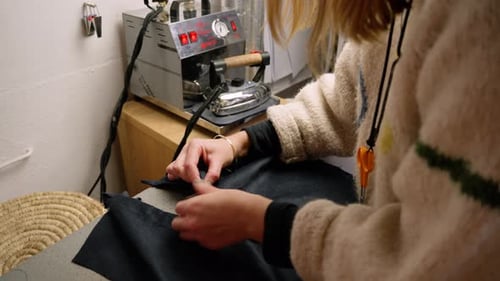 Seamstress sewing button onto clothing top. Wide shot.