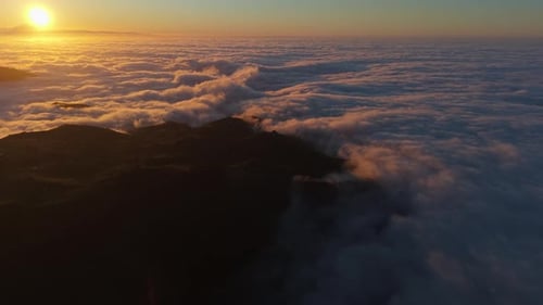 Fantastic drone shot orbiting over a sea of clouds at sunset, with the setting sun positioned next t