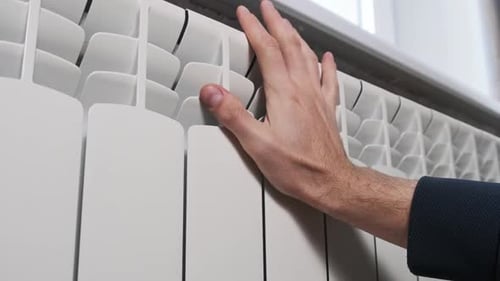 The Male Hand Touches a Cold Heating Radiator Against the Wall at Home