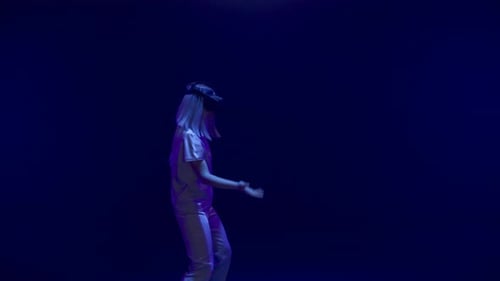 Blonde Woman Interacting with VR Headset in Dark Studio