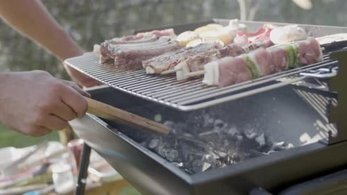 Barbecue Grill with Meat and Man Stirring and Blowing Out Coal