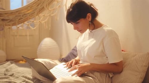 Junge schöne Frau sitzt auf dem Bett und benutzt Laptop zu Hause