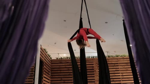 Young Woman in a Red Athletic Suit Does Complex Exercises on the Canvas Aerial Gymnastics in the