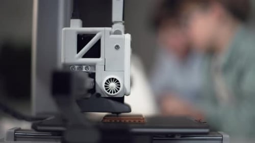 3D Printer in Operation in the Foreground with Kids on Background