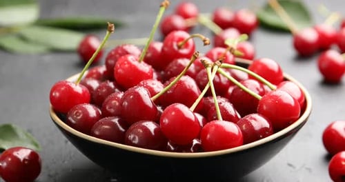 Spraying water onto ripe cherries at black table, closeup