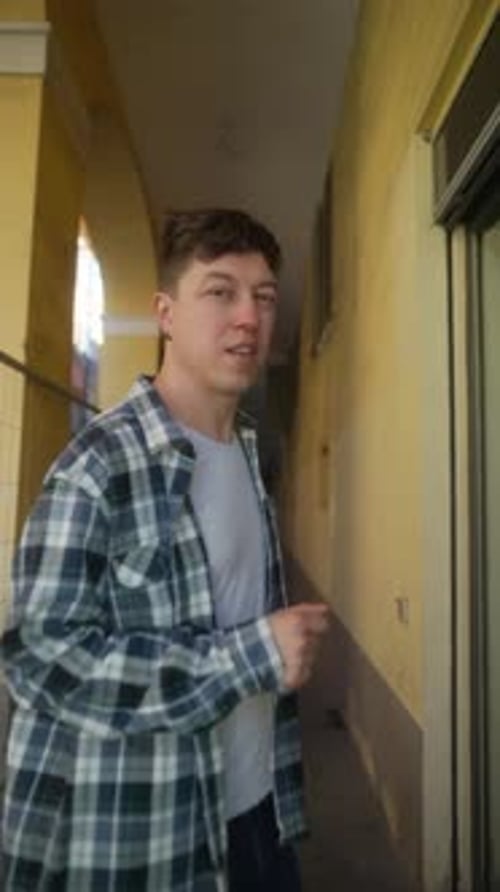A Young Man is Strolling in an Urban Area Wearing a Plaid Shirt and Jeans Exploring the Cityscape