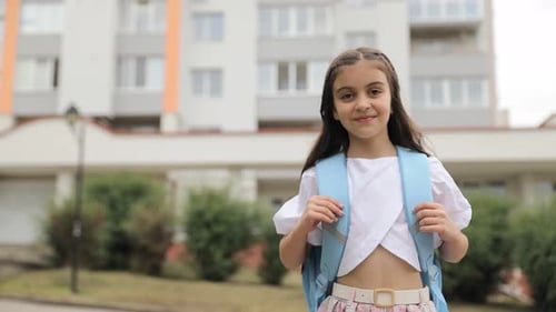 A Teenage Girl with a Backpack on Her Shoulders Returns From School Walking Through a Green Park