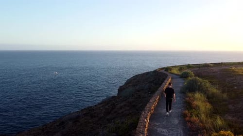 Young caucasian male walking away from camera on coastal cliff path