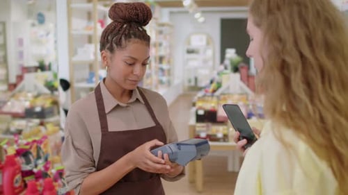 Cosmetics Store Worker Giving Payment Terminal to Female Client with Smartphone