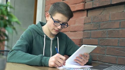 Happy Teenager with Smartphone and Notepad Doing Homework by Table in Cafe Adolescent