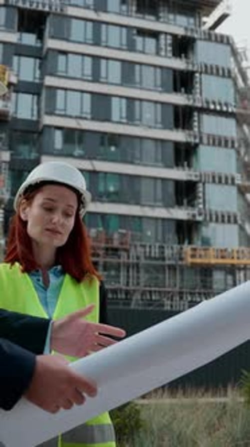 Dos arquitectos, trabajadores de la construcción, una mujer caucásica, un ingeniero, discuten el plan de construcción de una mujer