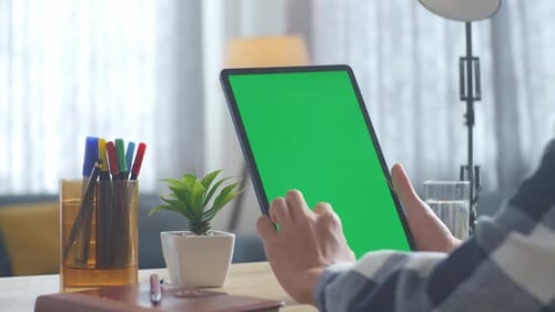 Close up of man's hand using a mock up green screen tablet on a desk