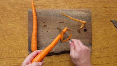 Hands Peeling Carrots on a Wooden Cutting Board