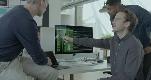 Three Male Engineers looking at Code on Computer Monitor in Office