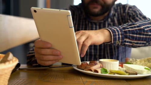 Young man browsing social media on tablet computer while eating breakfast