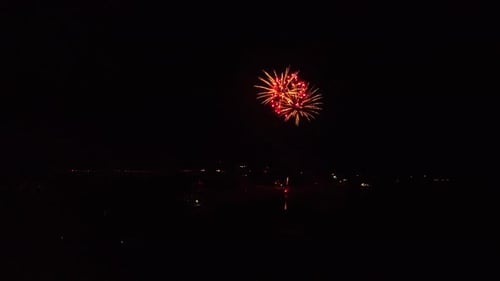 Long slow moving clip as drone is slowly flying towards exploding fireworks show over lake to see be