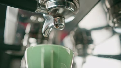 Pouring coffee flows from the machine into the cup making hot drink using the filter holder freshly