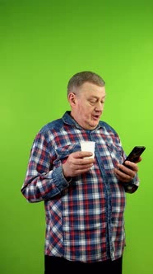 Adult Man Uses Smartphone While Holding Cup