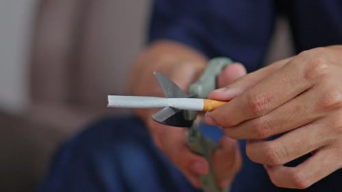 Nahaufnahme der Hände mit einer Schere, um die Zigarette in zwei Hälften zu schneiden