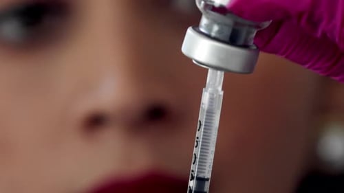 Female doctor or nurse fills a syringe from a vial of medication - close up