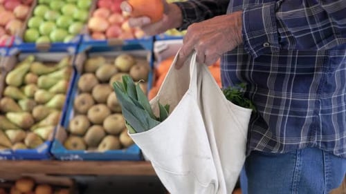 Nahaufnahme eines glücklichen älteren Mannes, der im örtlichen Marktladen eine wiederverwendbare Tüte mit frischem Gemüse in der Hand hält - Zero Waste