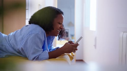Woman Lying on Bed Using Smartphone and Smiling