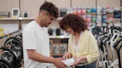 Happy couple choosing robot vacuum cleaner in electronics store in slow motion