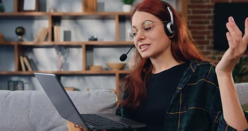 Mujer sonriente con auriculares con computadora portátil sentada en el sofá de casa.