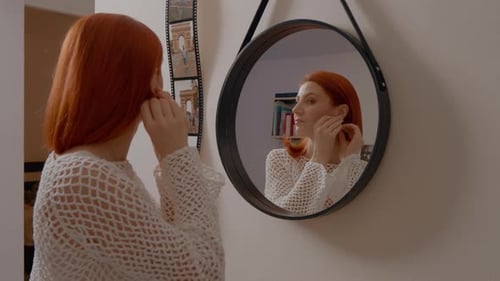 Woman Puts In Earrings Looking in Mirror