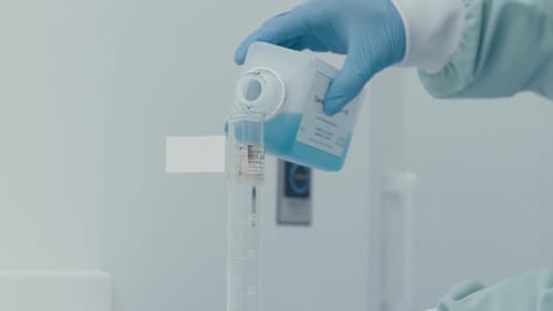 Lab worker's hand pouring serum liquid into Measuring Tube while working in Medical Drug Production