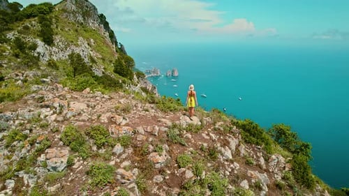 Woman admiring the seascape on mountain top of Capri island. The rocky cliffs with greenery, framing