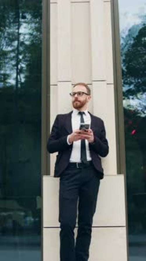 Stylish Handsome Businessman Holding Phone Reading Email Stands on Street in City Business District