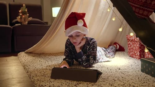 Boy with Santa Hat Plays Tablet in Christmas Tent