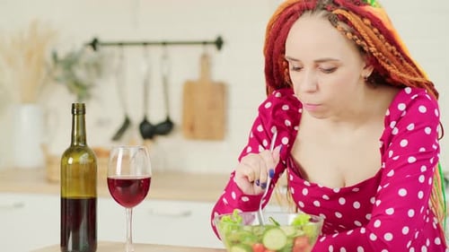 Woman Eats Salad with Wine in Kitchen