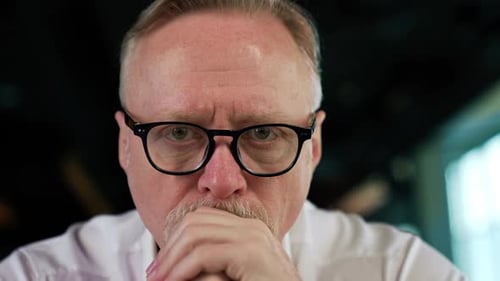 Focused strict serious face of a senior Caucasian man with fair hair in glasses.