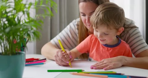 Woman and Child Drawing Together at Table Indoors