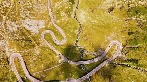 Green slopes of the road crossed by the wavy road and narrow river.