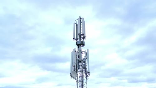 4G And 5G Antenna Of A Telecommunication Tower Against Bright Sky With Clouds. low angle orbit