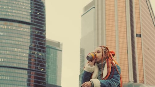 Young Woman with Orange Braids Drinks Beverage in City