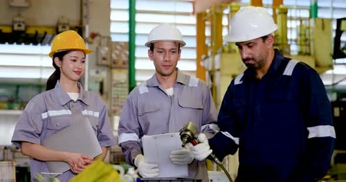 Asian female technician and two adult male engineers review tablet and paper near production area,