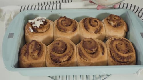 Icing Freshly Baked Cinnamon Rolls in Baking Dish