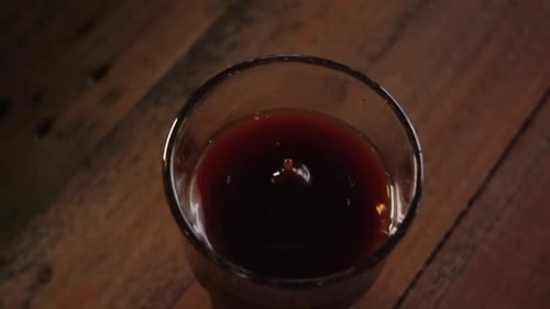 Coffee drop falls in to glass filled with coffee on wooden table, slowmo