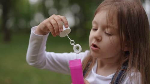 A Joyful Child is Playing with Bubble Solution Outside in a Beautiful and Sunny Garden