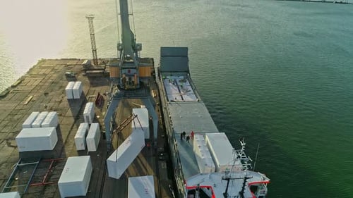 Aerial drone rotating shot over workers loading a container ship with white containers at daytime in