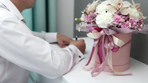 A young man in a suit writes a love note to his beloved. Close-up hand shots near a bouquet