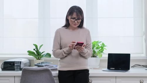 Woman Using Phone While Standing at Desk Indoors